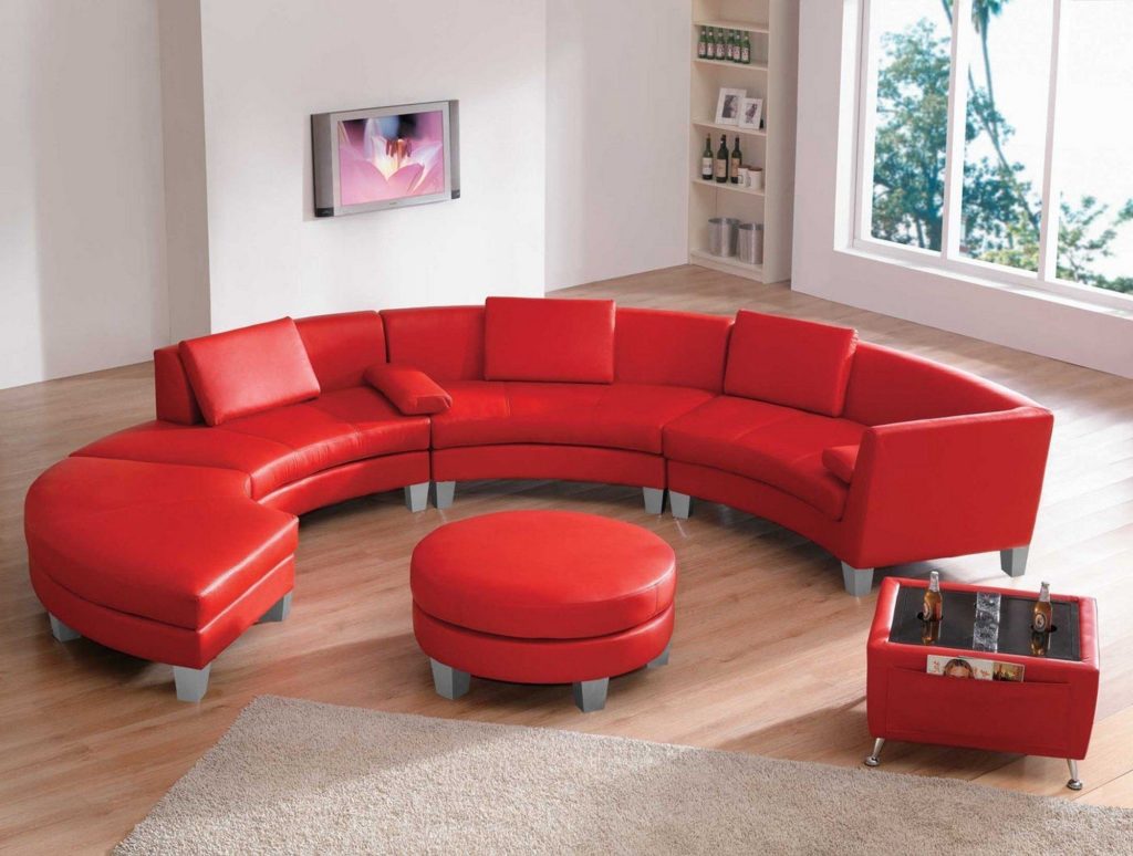 Красный радиусный диван в интерьере с круглым пуфиком